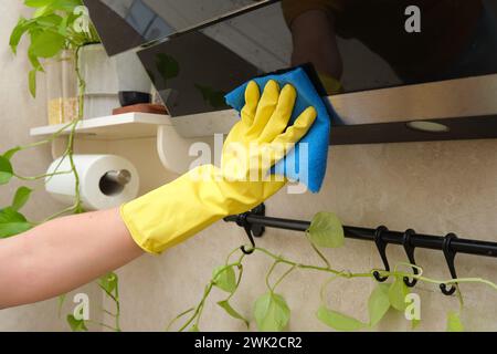 A woman washes the hood in her home kitchen with a rag. Female hands in yellow gloves while cleaning the kitchen Stock Photo