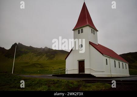 Front view of Vìk white church with red roof in south coast of Iceland, with mountains in background Stock Photo