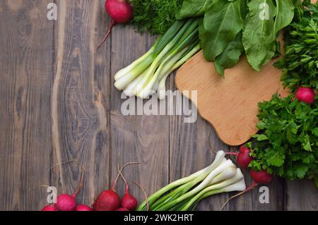 Helathy vegan food cooking background. Flat-lay of fresh tomatoes, radishes, parsley, spinach, dill, cilantro, sorrel, over wooden table, top view, co Stock Photo