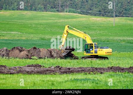 An excavator digs a trench to lay pipes in the soil Stock Photo