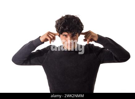 Too much noise: attractive young man covering his ears. A young man with curly hair is seen wearing a black sweater. He is standing against a neutral Stock Photo