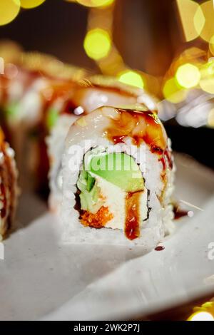 Sushi roll with scallop, cream cheese, masago and avocado against festive lights Stock Photo