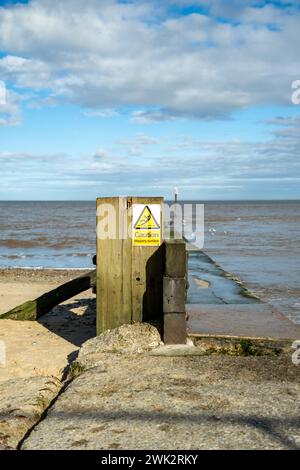 Warning sign on a concrete jetty on Mundesley beach, Norfolk coast Stock Photo