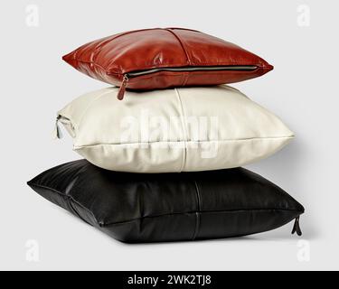 Stack of stylish minimalist square pillows of different sizes in black, white, and brown genuine leather with visible side zippers on light background Stock Photo