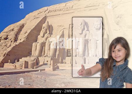 Little tanned girl is pointing a finger at a blank smartphone screen with famous temple in Abu Simbel in Egypt in the background. Travel concept with Stock Photo