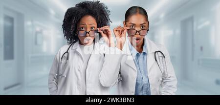 Two surprised female doctors in lab coats are adjusting their glasses in a hospital Stock Photo