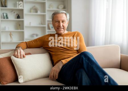 Handsome grandfather sitting on couch at home, smiling at camera Stock Photo