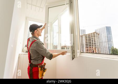 The installer worker in safe medical mask and overalls fixes a detail of the stiffener element with screws using an electric screwdriver to the wall Stock Photo