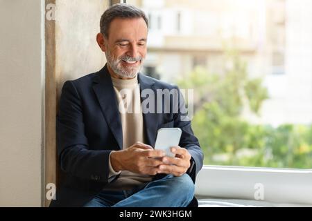 Smiling older man using a smartphone by the window Stock Photo