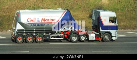 Civil & Marine Slag Cement business logo brand on historical archive view of a hgv lorry articulated tanker semi-trailer truck combination vehicle with raised economy axle driver at work driving along M25 motorway road London orbital route on Essex section England UK Stock Photo