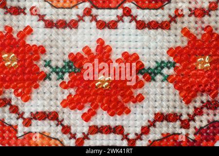 A close-up shot of a cross stitched ornament with red beads flowers made with white and red threads. Stock Photo