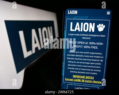 Person holding cellphone with webpage of Large-scale Artificial Intelligence Open Network (LAION) with logo. Focus on center of phone display. Stock Photo