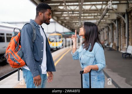 a young couple swearing and argueing with each othe at the train station on the platform The concept of disagreements in the family Stock Photo
