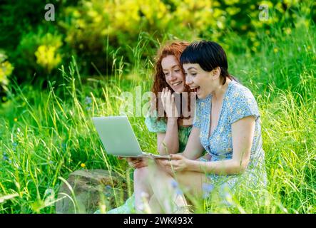 two friend, girlfriend and women using laptop, having videochat, watching video in public park. Romantic concept Internet anywhere Stock Photo