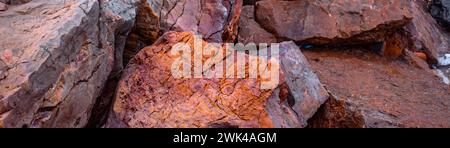 Seaside textured red rocks concept photo. Wide banner of rough surface. Panoramic Mediterranean sea close up stones. High quality picture for wallpape Stock Photo