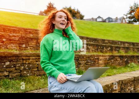 Portrait of beautiful happy young woman graduate with curly red hair talking on the mobile and excited  about news regarding her job application Stock Photo