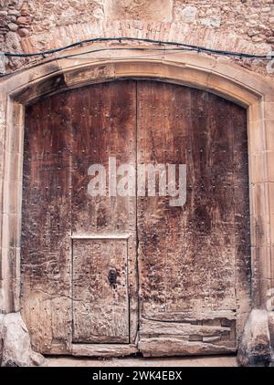 Brown wooden old door made from slats photo. Gray brick wall medieval house. Entrance with keyhole and iron fittings in a stone wall. Typical architec Stock Photo