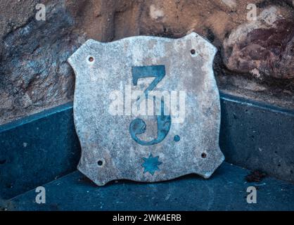 Gray house number plate in Catalonia. Street sign number 3 on old textured wall. Street scene. High quality picture for wallpaper, article Stock Photo