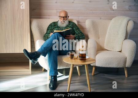 Old man sits comfortably with a book in a comfortable chair Stock Photo