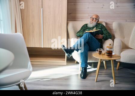 Pensioner sits down with a book in a comfortable chair Stock Photo
