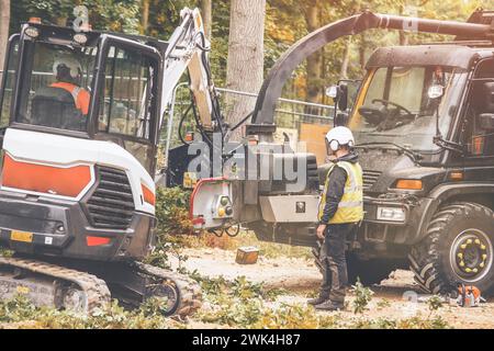 Arborist using a wood chipper machine for shredding trees and branches. The tree surgeon is wearing a safety helmet with a visor and ear protectors Stock Photo