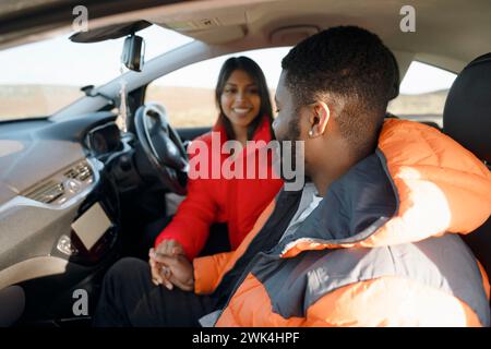 Beautiful happy young loving couple holding hands and smiling while sitting in their first car. Buy your first car concept Stock Photo