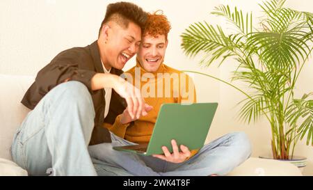 Gay couple laughing while using a laptop on the sofa Stock Photo