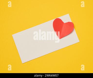 Rectangular white paper envelope and red heart on a yellow background, holiday background Stock Photo