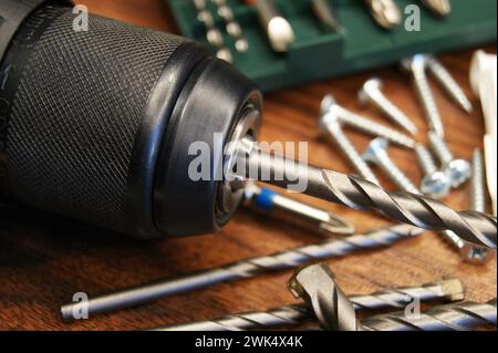 Close-up of a drill, set with drills and various materials on a wooden background. Stock Photo