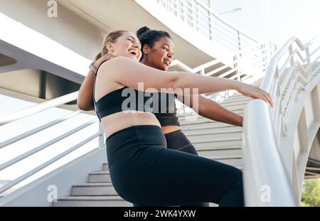Two sportswomen having fun while standing at railing on the bridge after an intense workout. Female friends in sportswear enjoying a good mood after e Stock Photo