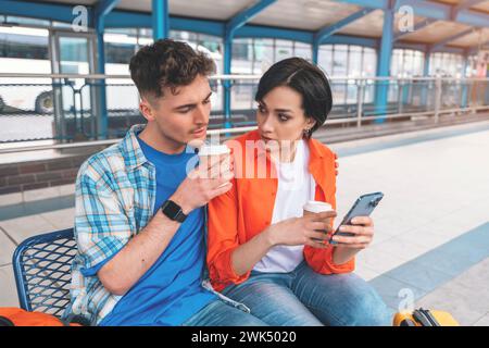 a young couple traveling together during their honeymoon, sitting in Interchange, waiting for bus, drinking coffee, chatting, reading news. Traveling Stock Photo