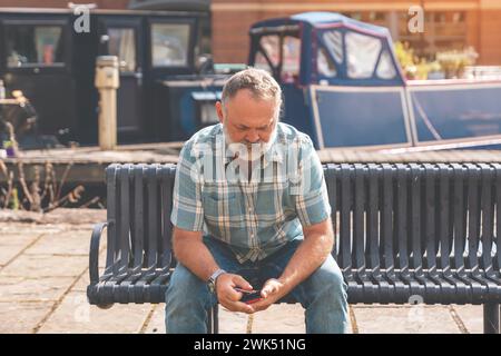 Mature man sitting on a bench and using a smartphone Stock Photo