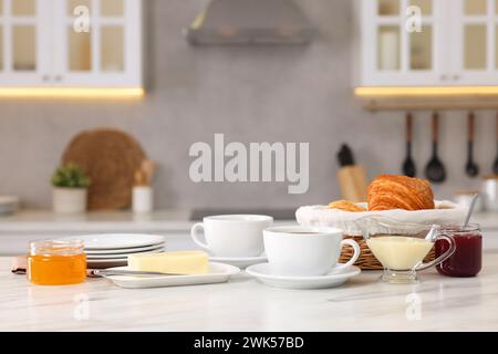 Breakfast served in kitchen. Fresh croissants, coffee, butter, jam, honey and sweetened condensed milk on white table Stock Photo