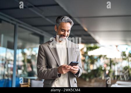 Happy mature older male entrepreneur standing outdoors using smartphone. Stock Photo