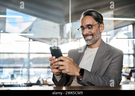 Smiling mature business man executive sitting at desk using smartphone. Stock Photo