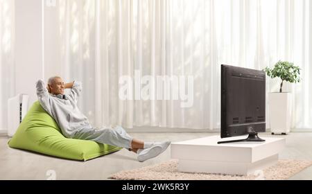 African american guy sitting on a green bean bag armchair and watching tv in a modern minimal living room Stock Photo