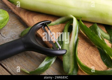 Fresh cucumber, peels and peeler on wooden table, closeup Stock Photo