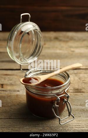 Tasty barbeque sauce in jar and spoon on wooden table Stock Photo