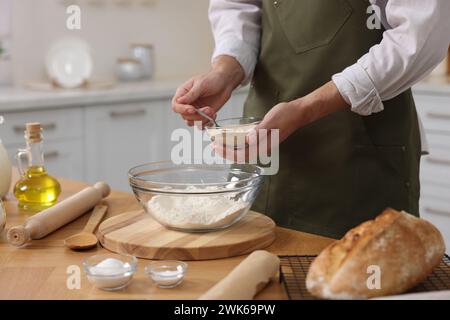 Making bread. Man putting dry yeast into bowl with flour at wooden table in kitchen, closeup Stock Photo