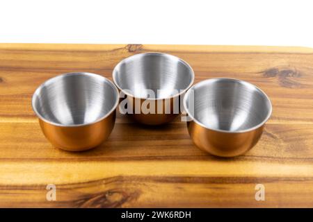 Three copper and silver bowls on a wooden cutting board Stock Photo