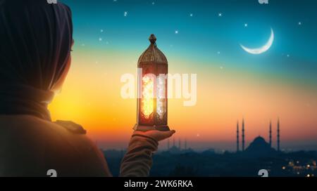 Woman is holding Ornamental Arabic lantern with burning candle glowing at night mosque background. Festive greeting card, invitation for Muslim holy m Stock Photo