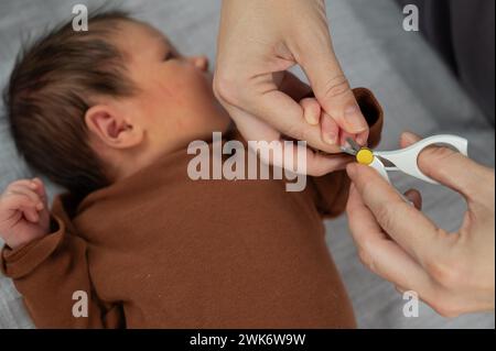 Mom cuts her newborn son's fingernails with small children's scissors. Stock Photo