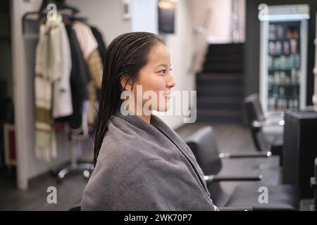 Woman with wet hair sitting wrapped in towel at salon Stock Photo