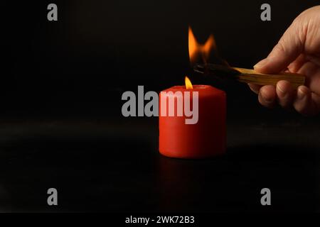 A woman lights a holy stick, palo santo, with a red candle flame isolated on a black background Stock Photo