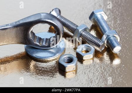 Ring wrench, nuts and bolts on golden metal surface close up Stock Photo