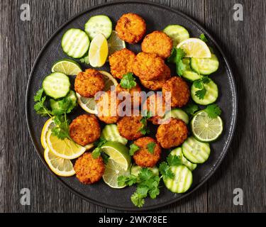 fried rice cakes, rice tikki, indian style on black plate served with cucumber, lemon, lime slices on dark wooden table, flat lay, close-up Stock Photo
