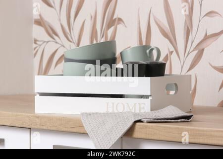 Ceramic bowls and mugs in the wooden box on the kitchen counter, domestic life organization concept Stock Photo