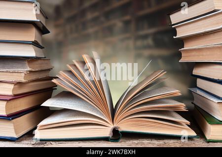 A stack of old books on a wooden surface against a background of bookshelves Stock Photo