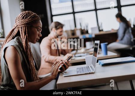 Beautiful businesswoman working on laptop in modern office. Group of freelancers working in shared work area. Concept of coworking, common workspaces Stock Photo