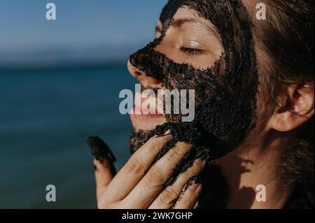 Woman applies healing mud to her face and body. Natural healing mud in Croatia on the beach. Therapeutic mud or peloids rich in minerals and organic s Stock Photo